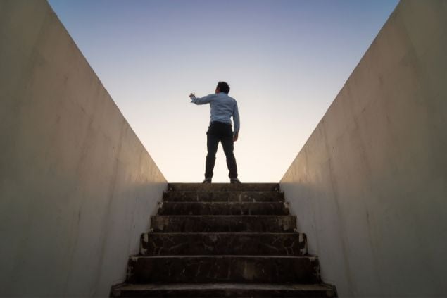 Imagem de um homem no topo da escada com o braço levantado em direção ao céu