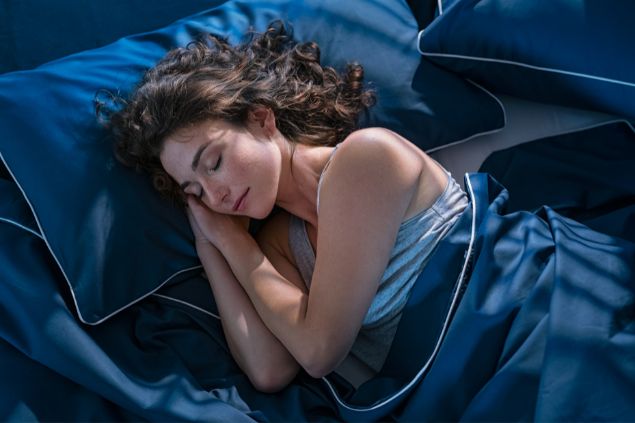Imagem de uma mulher dormindo tranquilamente em sua roupa de cama azul escuro