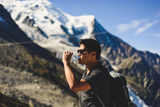 Homem branco com garrafa de água na boca nas montanhas.
