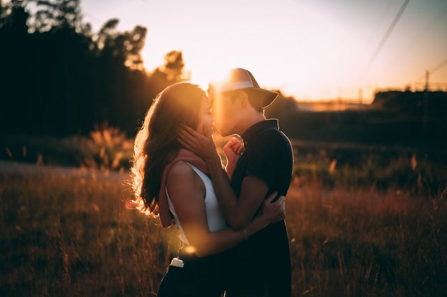 Mulher e homem brancos se beijando num campo.