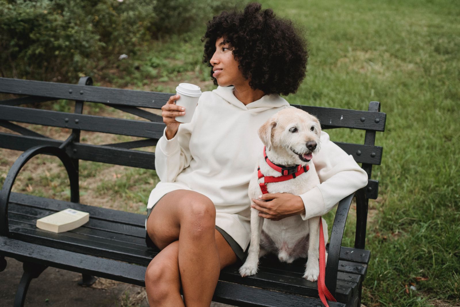 Mulher sentada em uma cadeira da praça segurando um café ao lado de seu cachorro