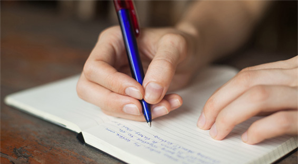 Mão segurando uma caneta e escrevendo sobre um caderno