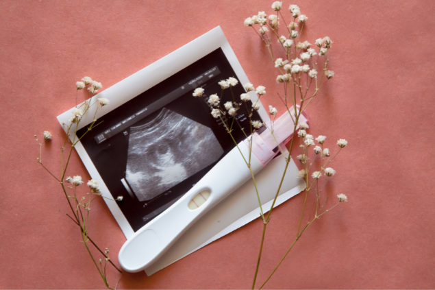 Teste de gravidez e foto de ultrassom com raminhos de flores.