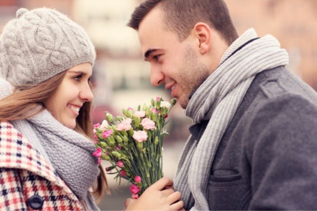 casal se olhando nos olhos e sorrindo e a mulher está segurando um buquê de flores