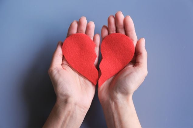Imagem só das mãos de uma pessoa, segurando um coração partido feito de papel vermelho