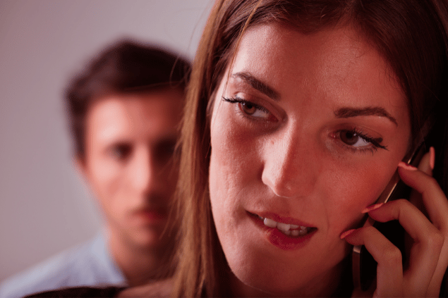 Homem ao fundo sentindo ciúmes de uma mulher, enquanto ela conversa no celular. 