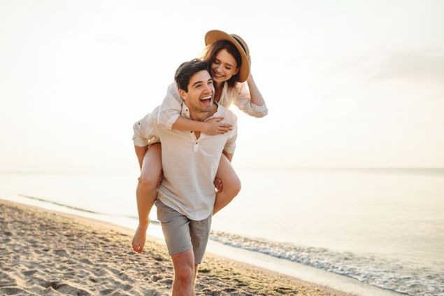 Casal feliz e sorrindo enquanto andam de cavalinho na praia
