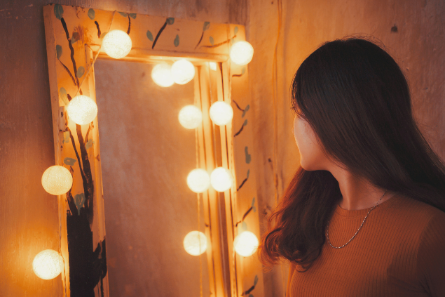 Mulher se olhando em um espelho com várias luzes em volta