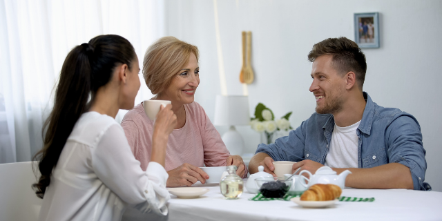 Duas mulheres e um homem têm refeição, eles estão sentados à mesa e sorriem.