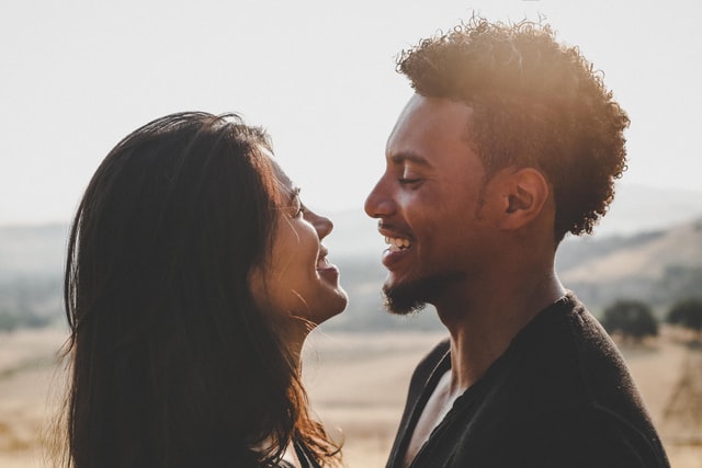 Homem negro e mulher branca sorrindo um para o outro.