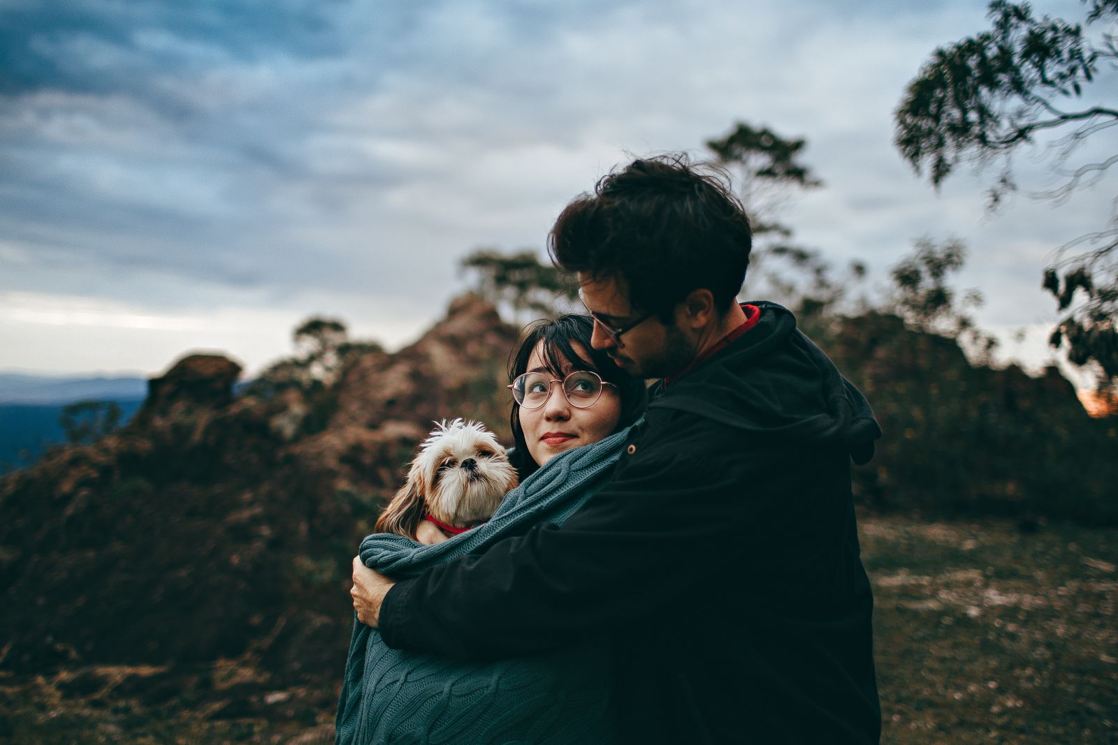 Homem abraçando mulher a sua frente que está segurando um cachorrinhi